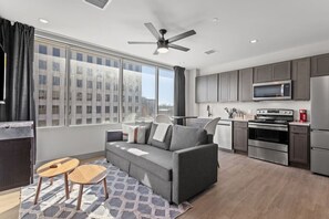 A modern apartment with a grey sofa, a small wooden table, a kitchen with grey cabinets, a microwave, and a stove. - 175 LEX - Loft in Downtown Lexington, Rupp Arena (Lexington)