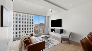 A modern living room with a large window, a flat-screen TV, a sofa, a chair, and a coffee table. - 175 LEX - Walkable Downtown Lexington Condo (Lexington)