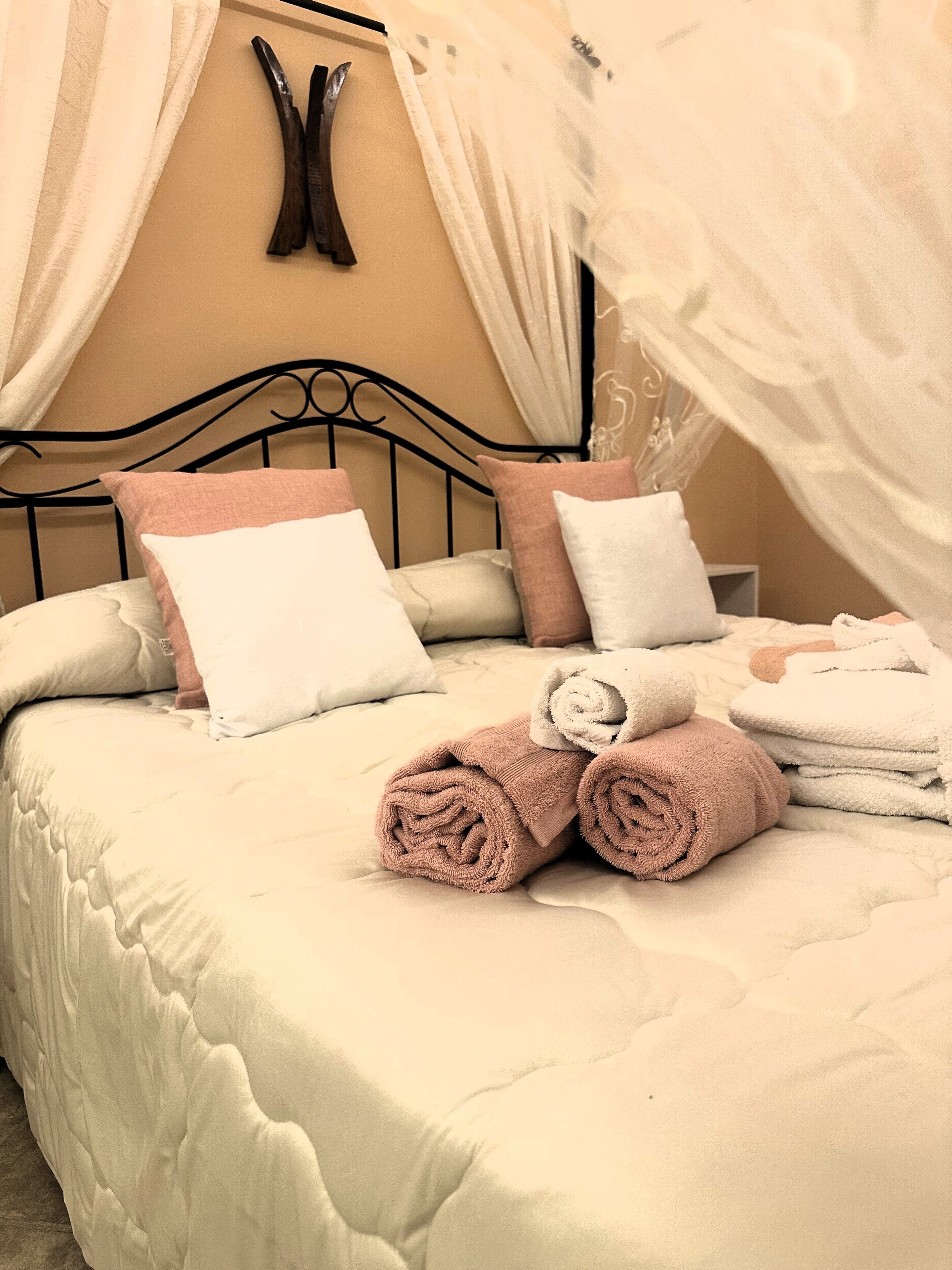 A neatly made bed with rolled towels, a canopy, and a headboard.