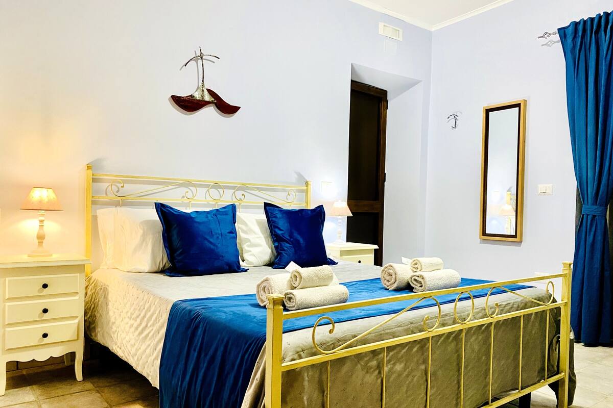 Un lit avec un cadre en métal, des commodes blanches, une table de chevet avec une lampe et un miroir accroché au mur.