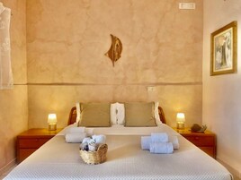 Habitación de hotel con una cama grande, dos mesitas de noche, una lámpara fijada a la pared y un cuadro enmarcado.