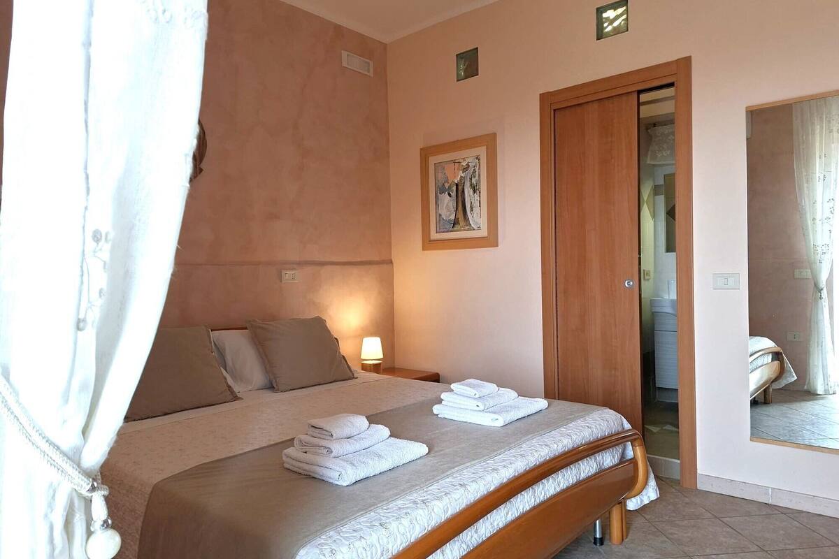 Une chambre à coucher avec un lit, des oreillers, une lampe de chevet, une porte et un miroir.