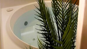 A bathroom with a bathtub, a wall-mounted light fixture, and a potted plant. - Agri Resort Masusa (Aquara)