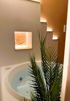 Un baño con bañera, lámpara de pared y planta en maceta.