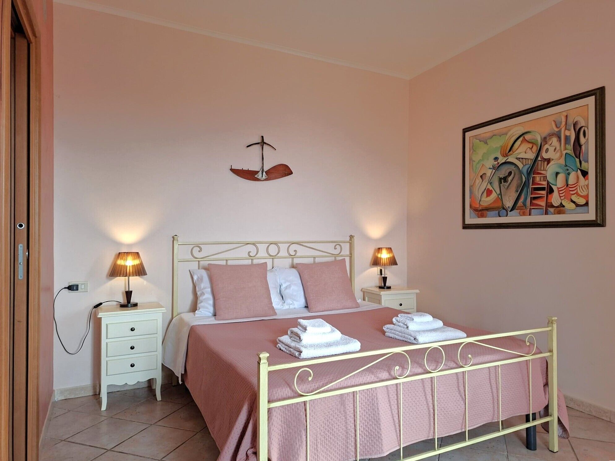 A bedroom with a bed, bedside tables, lamps, a painting, and a hanging light fixture.