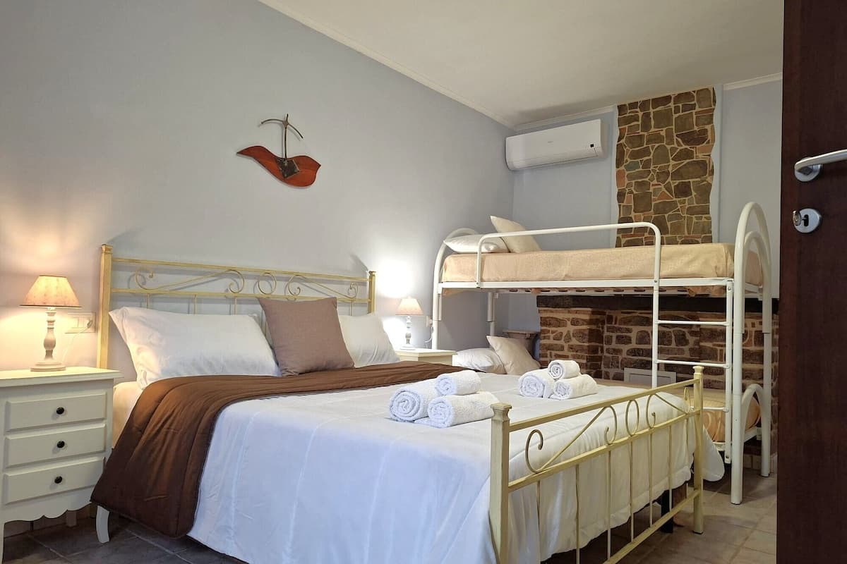 Une chambre avec un lit superposé, une table de chevet avec une lampe, un climatiseur mural et un mur en pierre.