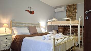 Una habitación con una cama litera, una mesita de noche con lámpara, aire acondicionado de pared y una pared de piedra.
