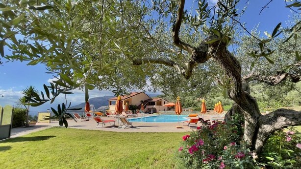 A pool area with lounge chairs and umbrellas, surrounded by greenery and a building in the background. - Agri Resort Masusa (Aquara)
