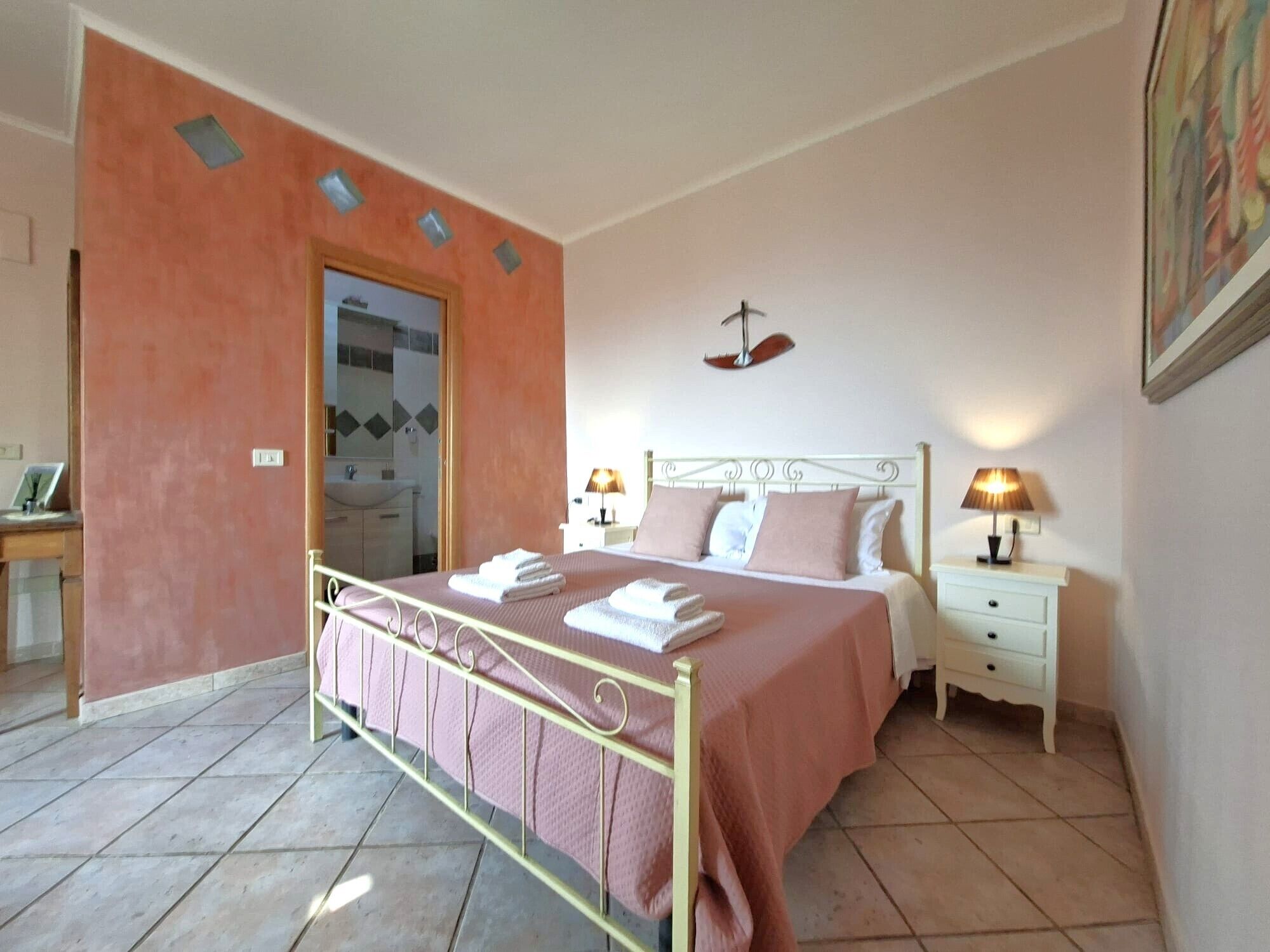 Een slaapkamer met een bed, nachtkastjes, een deur en een zichtbare badkamer door een open deur.