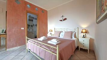 Een slaapkamer met een bed, nachtkastjes, een deur en een zichtbare badkamer door een open deur.