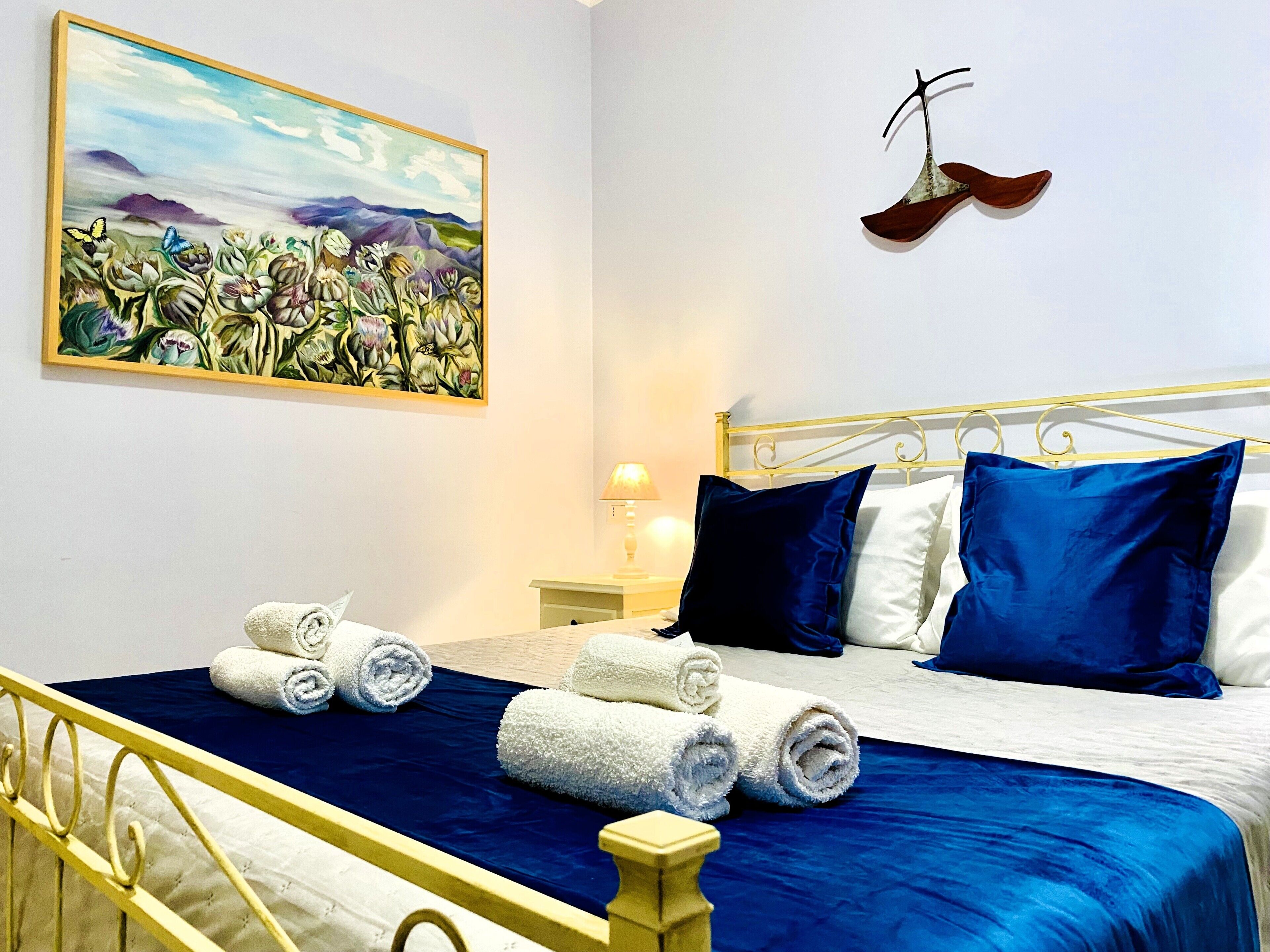 A hotel room with a bed, pillows, a painting, and a pair of shoes on the wall.