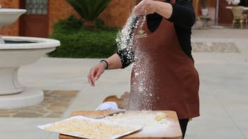 A person in a brown apron sprinkling flour on a wooden table outdoors.