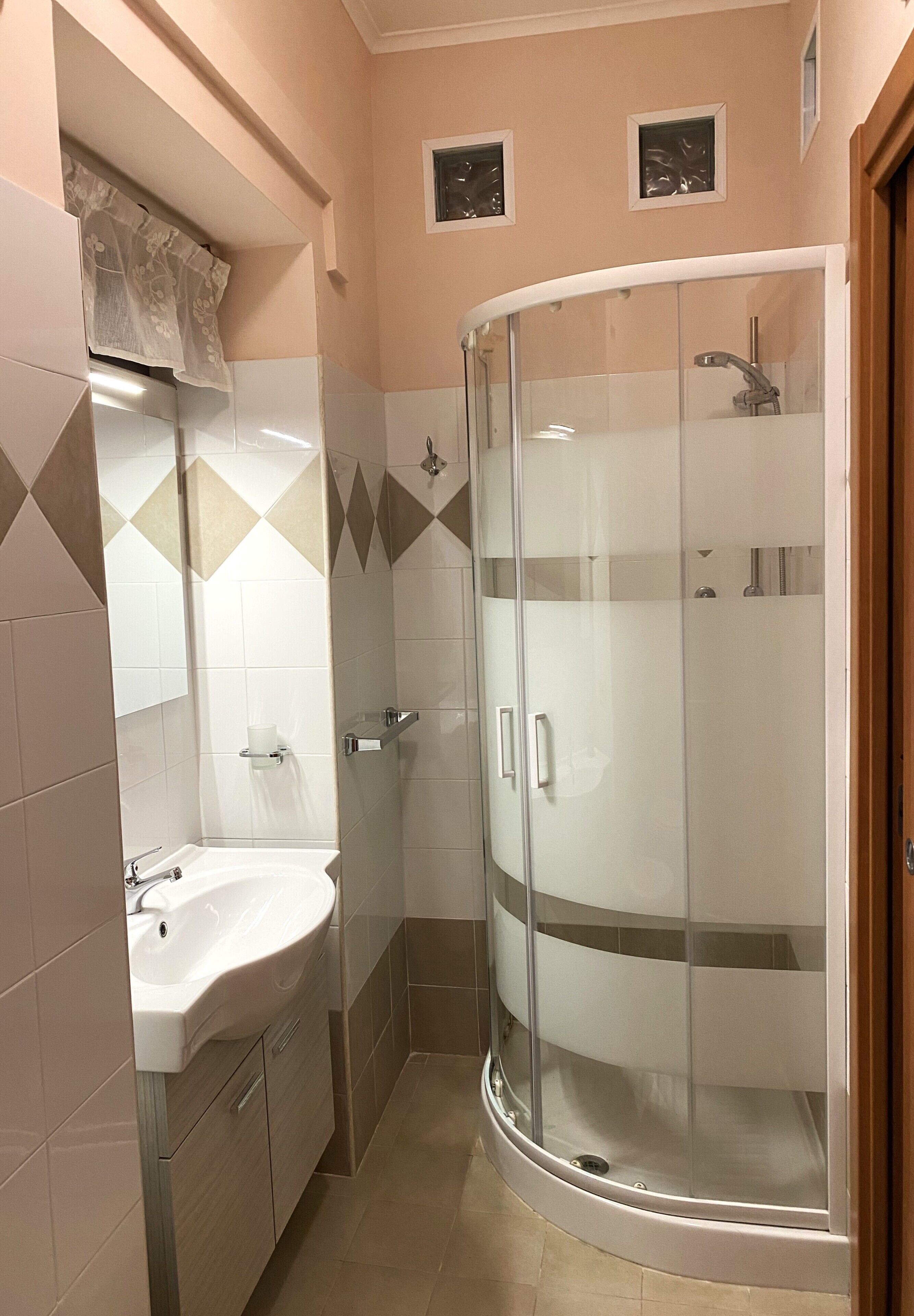 A bathroom with a glass-enclosed shower, a sink, and a mirror.