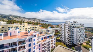 A coastal cityscape with modern buildings, a clear sky, and a view of the sea. - Casa Branca 360 - Penthouse - By Wehost (Funchal)