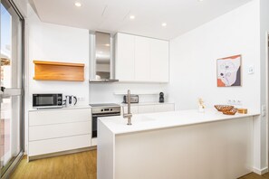 A modern kitchen with white cabinetry, a built-in microwave, a kettle, and a coffee maker.