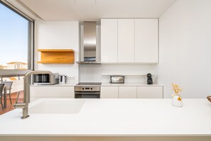 Una cocina moderna con muebles blancos, una campana extractora de acero inoxidable, un horno integrado y un microondas.