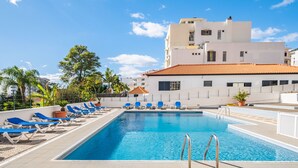 A swimming pool with blue lounge chairs and a building with a tiled roof in the background. - Casa Branca 360 - Penthouse - By Wehost (Funchal)