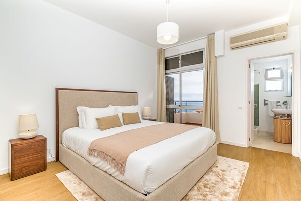 Un dormitorio con una cama grande, una mesita de noche, una ventana con vistas y un baño visible a través de una puerta abierta.