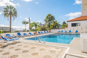 Una piscina con sillas reclinables azules y palmeras.
