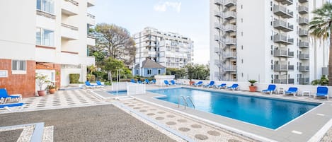 A swimming pool with lounge chairs, surrounded by multi-story residential buildings.