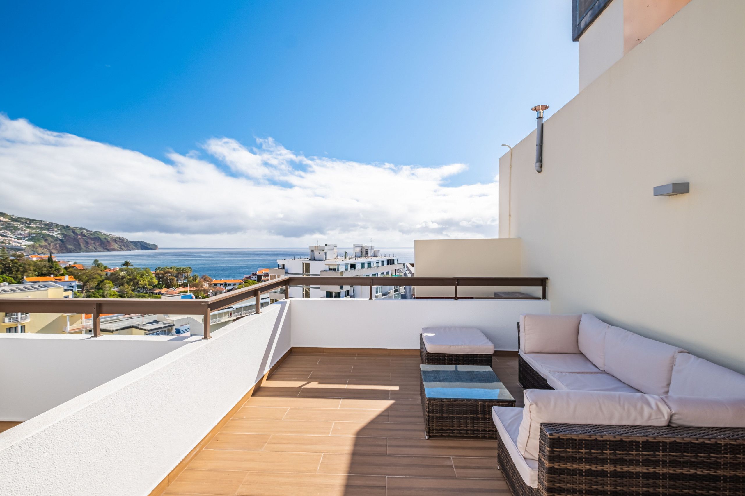 Un balcón con sofá, una mesita y vistas al mar y edificios.