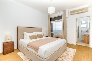 Un dormitorio con una cama grande, una mesita de noche, una ventana con vistas y un baño visible a través de una puerta abierta.