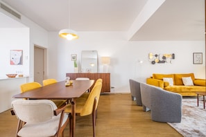 A modern living room with a wooden dining table, yellow chairs, a gray sofa, and a yellow couch.