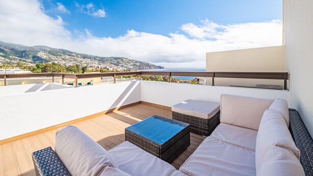 A rooftop terrace with a view of a coastal town and mountains. It includes a seating area with cushions and a table. - Casa Branca 360 - Penthouse - By Wehost (Funchal)