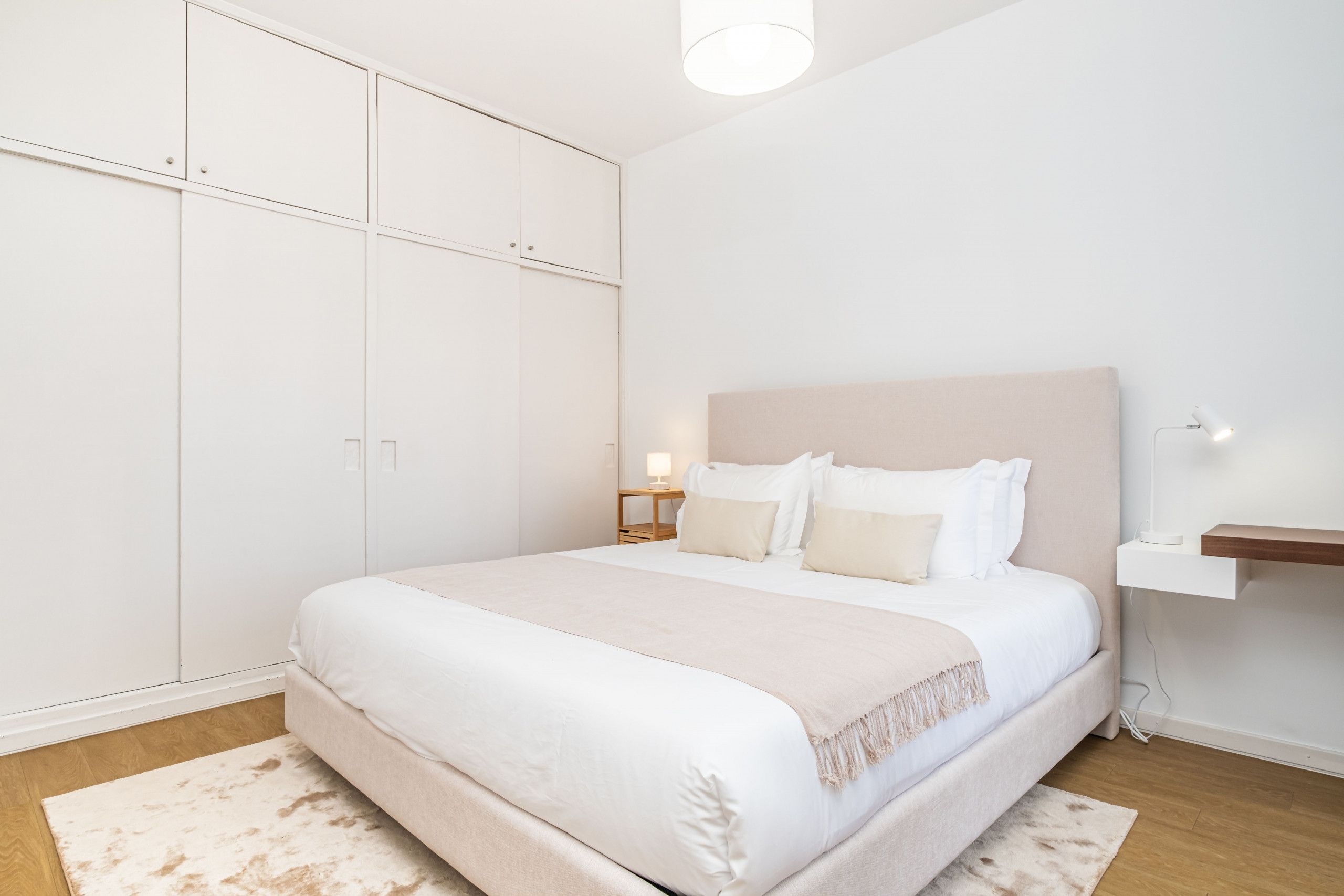 Un dormitorio con una cama grande, un armario, una mesita de noche con lámpara y una estantería en la pared.