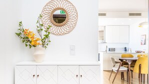 A modern kitchen with white cabinets, a round mirror, and a dining area with yellow chairs. - Casa Branca 360 - Penthouse - By Wehost (Funchal)