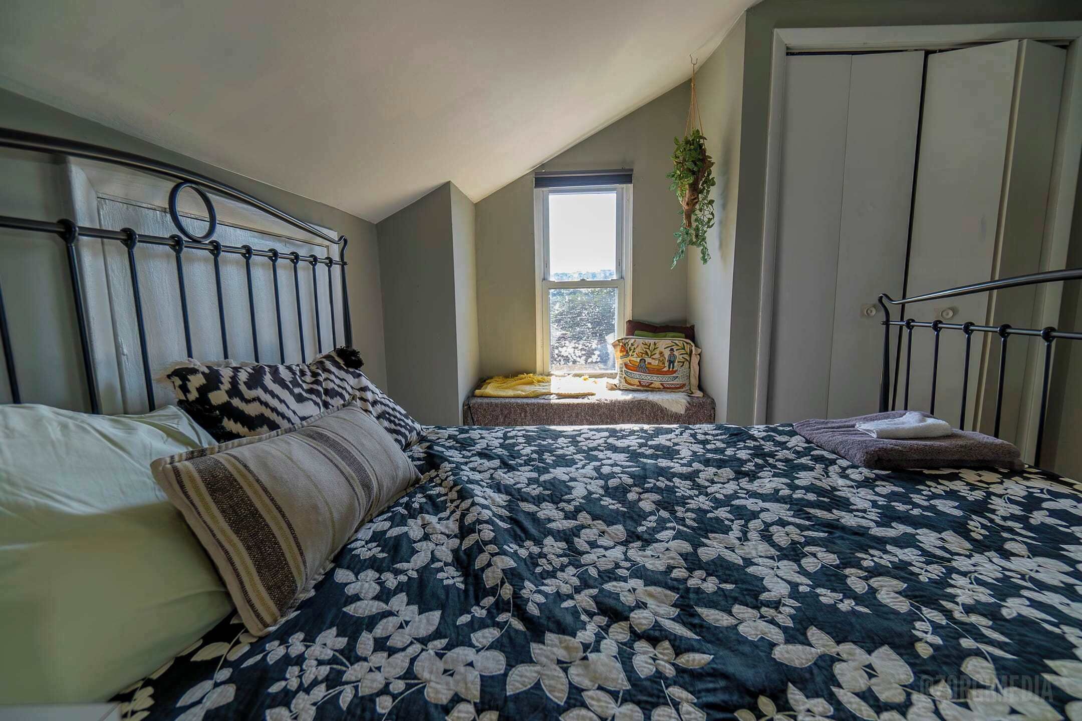 Un dormitorio con cama, ventana, planta colgante y armario.
