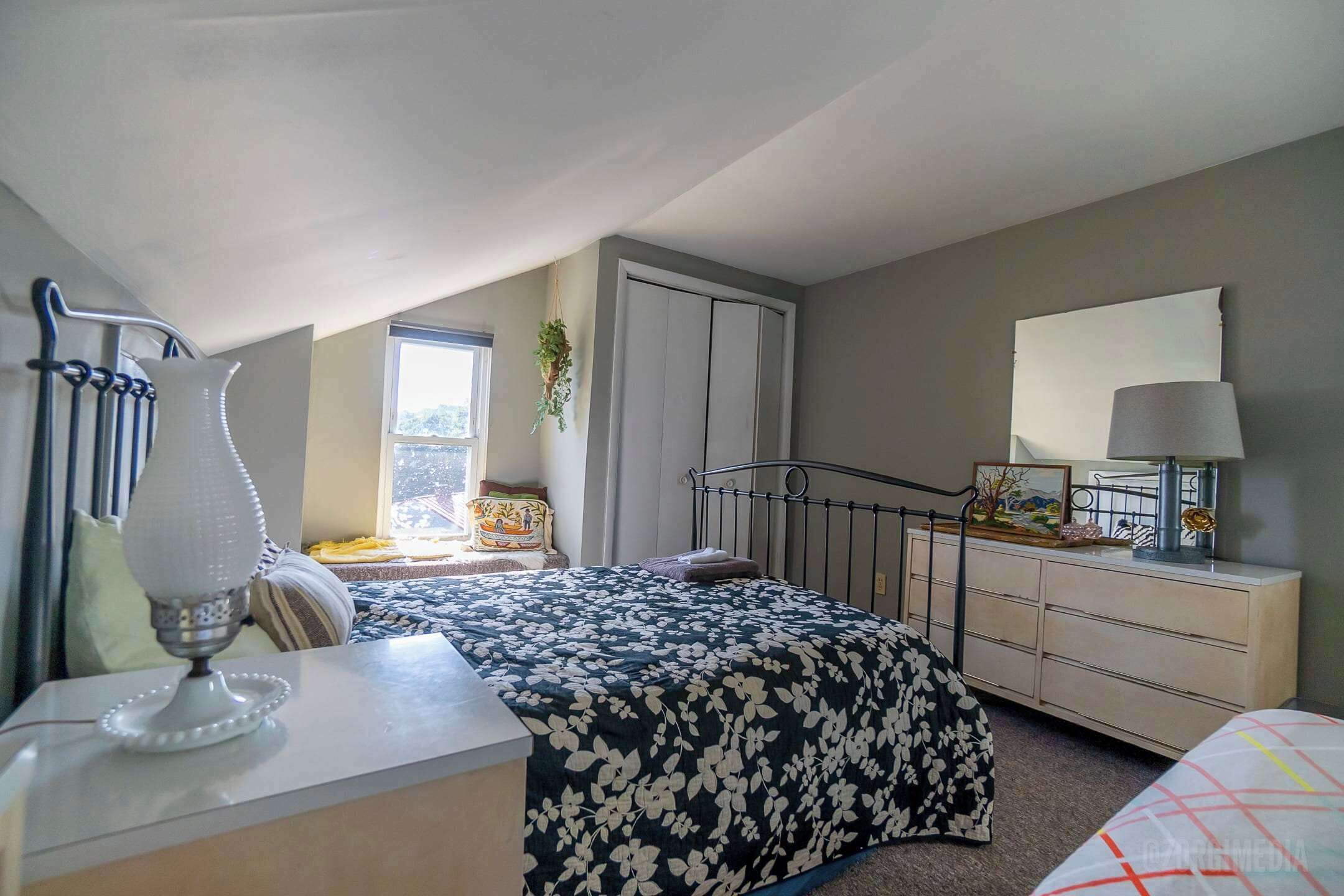Un dormitorio con cama, cómoda, lámpara y ventana con vistas.