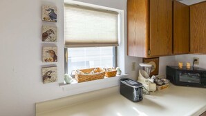 A kitchen with wooden cabinets, a window with blinds, a toaster, and a blender on the counter.