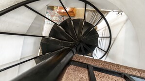 A spiral staircase with a black handrail and a white wall in the background.