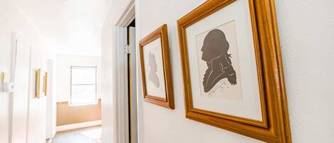 A hallway with framed artwork on the walls, a door leading to another room, and a red rug on the floor.