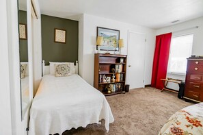 A bedroom with a bed, a bookshelf, a dresser, and a window with curtains.