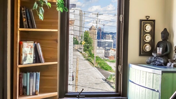 A room with a window overlooking a cityscape, a bookshelf, a Buddha statue, and a staircase. - Amazing Views- George Washington on Mt. Washington (Pittsburgh)
