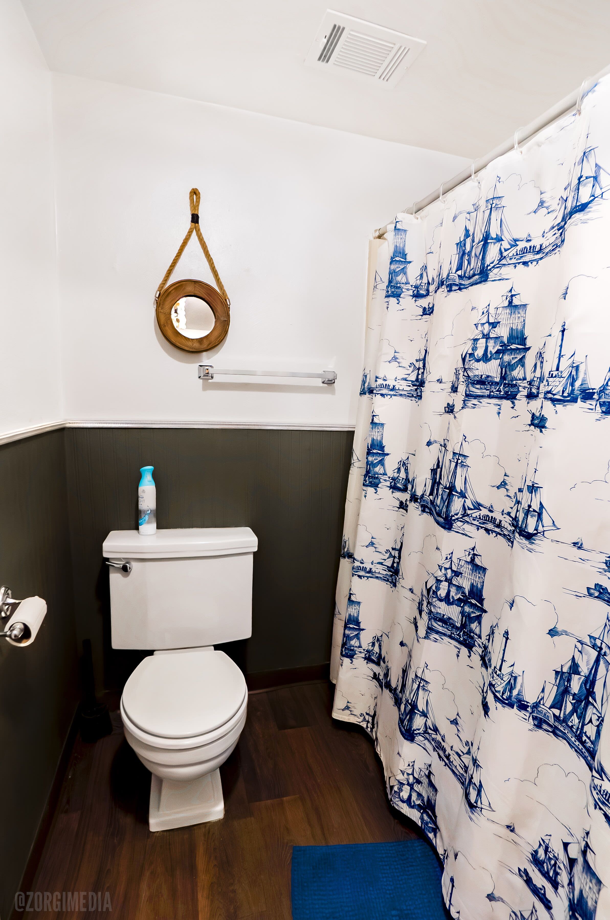 Een badkamer met een toilet, een handdoekhouder en een douchegordijn met een nautisch thema.