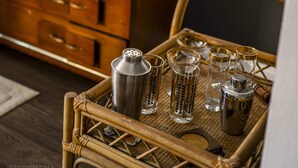 A wicker tray with cocktail shakers and glasses, a wooden dresser, a television, and a table lamp in a room. - Amazing Views- George Washington on Mt. Washington (Pittsburgh)