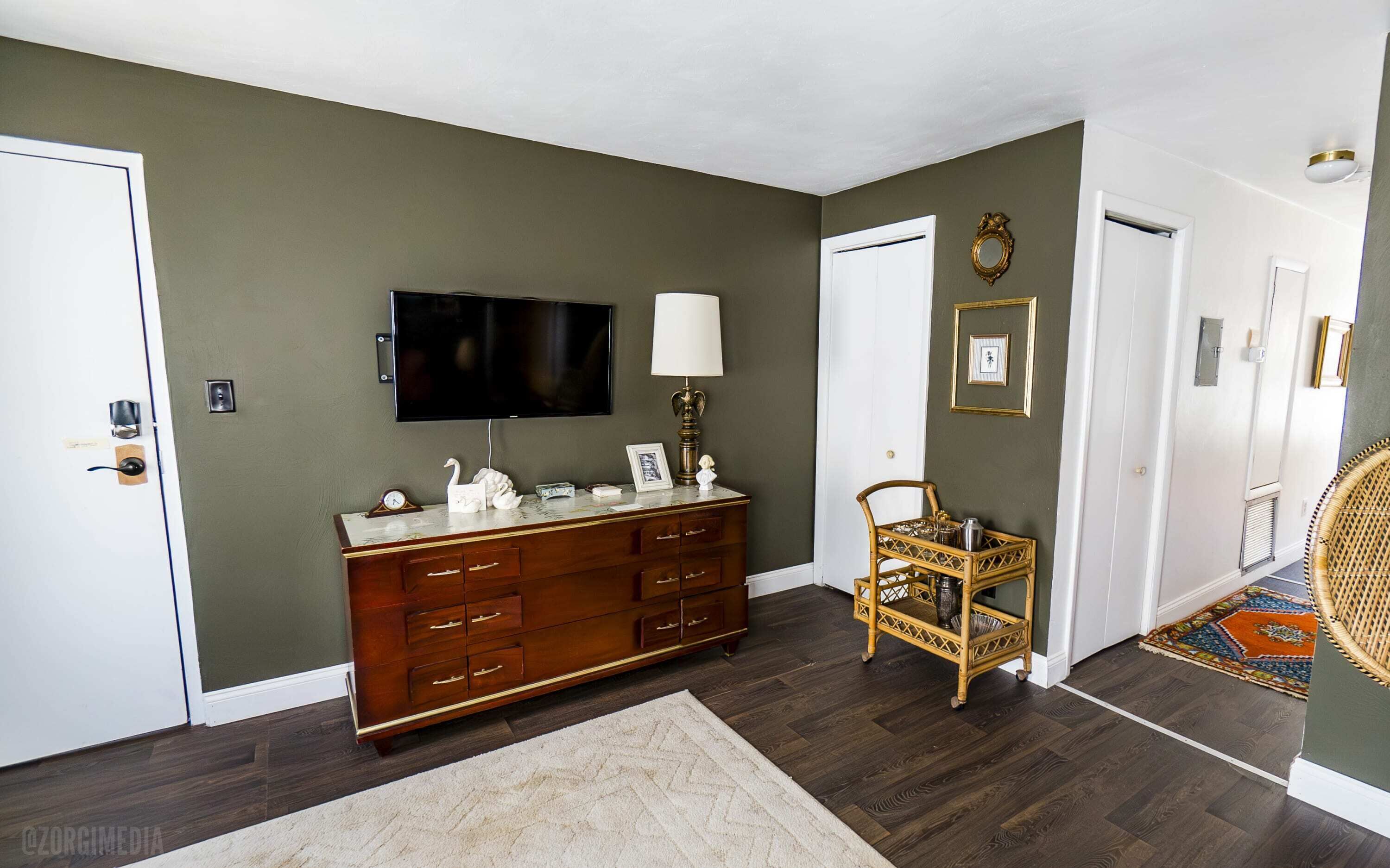 A room with a wooden dresser, a television, a lamp, and a wicker chair.