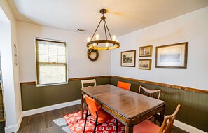 A dining area with a wooden table, orange chairs, a chandelier, and framed pictures on the wall.