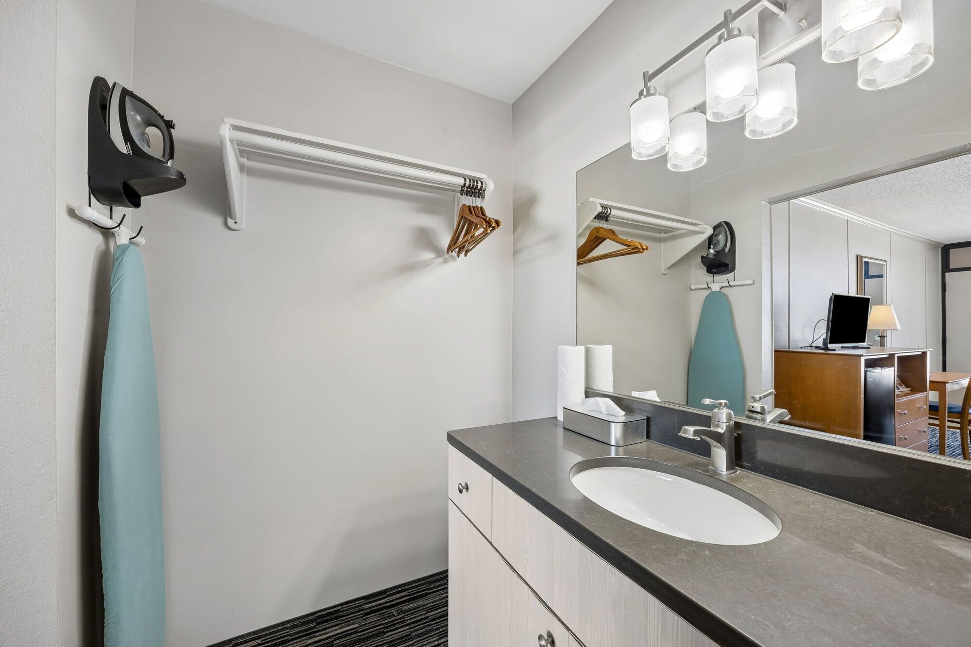 A modern bathroom with a sink, mirror, towel rack, and hanging clothes.