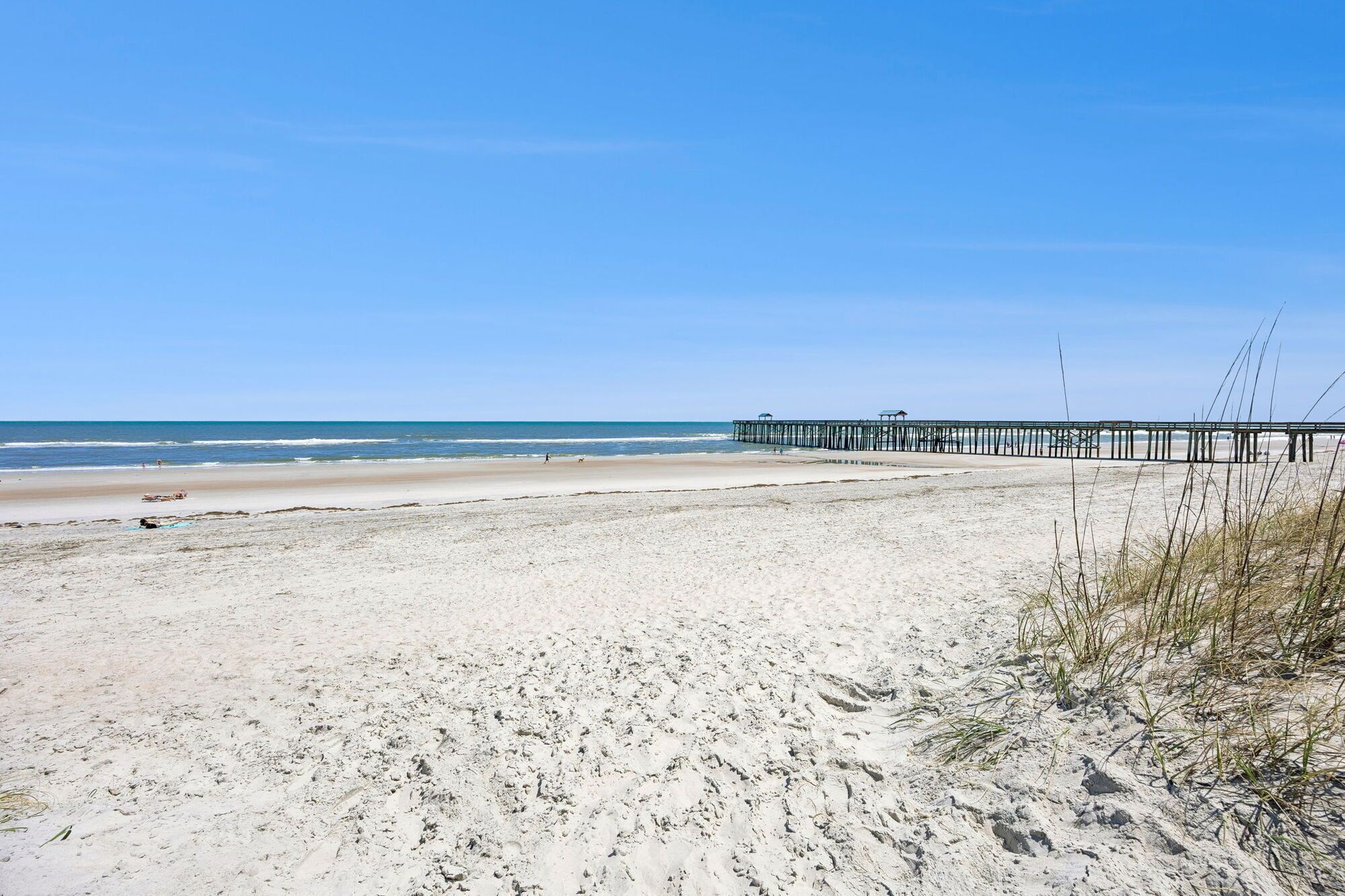 Une plage avec une jetée qui s’avance dans l’eau, une plage de sable et un ciel dégagé.
