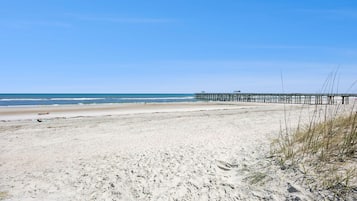 Une plage avec une jetée qui s’avance dans l’eau, une plage de sable et un ciel dégagé.