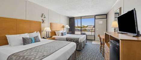 A hotel room with two beds, a desk with a TV, and a balcony with a view.