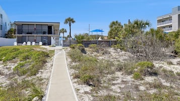 Un chemin menant à un bâtiment avec vue sur la plage, un parasol bleu et un panneau indiquant un emplacement en bord de mer.