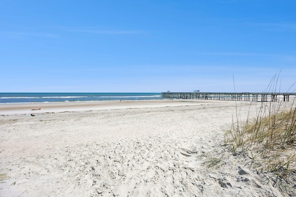 A beach with a pier extending into the water, sandy beach, and clear skies.