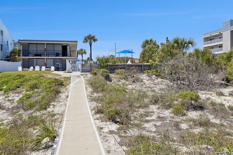 A pathway leading to a building with a beach view, a blue umbrella, and a sign indicating a beachside location.. Beachside Motel Deluxe Near Ocean