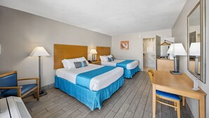 Et hotelværelse med to senge, et skrivebord, en stol, en lampe og et spejl.