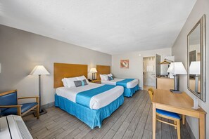 Et hotelværelse med to senge, et skrivebord, en stol, en lampe og et spejl.